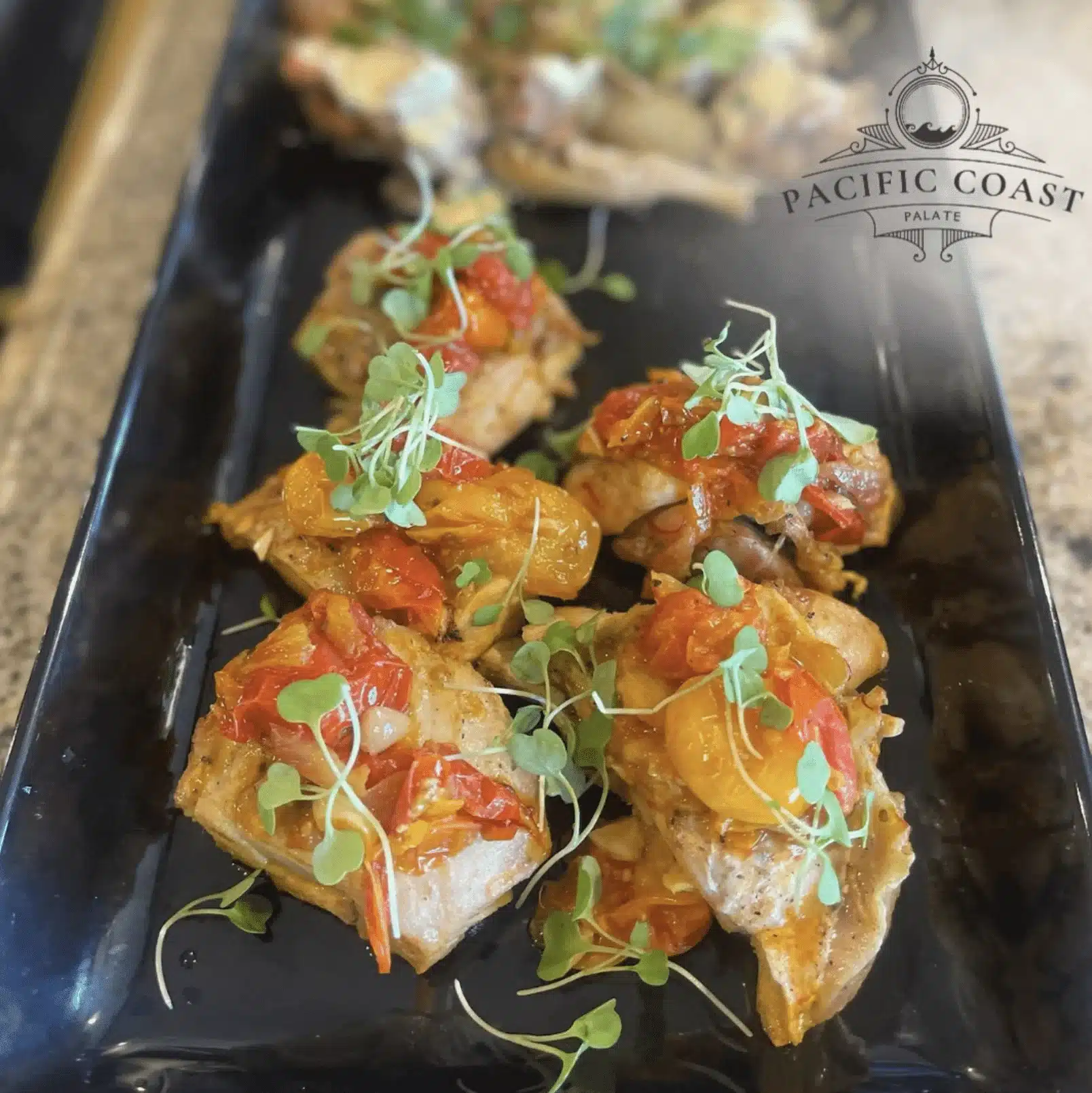 Individual food bites from Pacific Coast Palate, topped with roasted red and yellow tomatoes and fresh microgreens on a black serving platter.